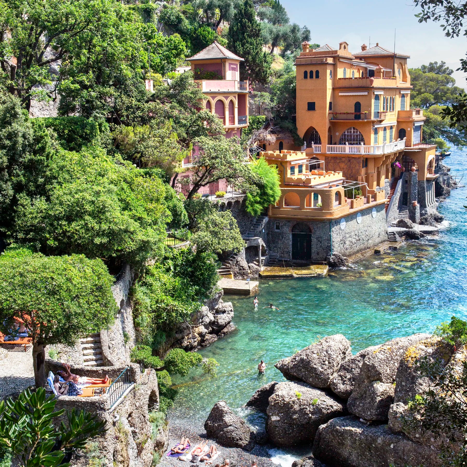 Luxurious waterfront villa with gardens and a pool, surrounded by trees and rocks.