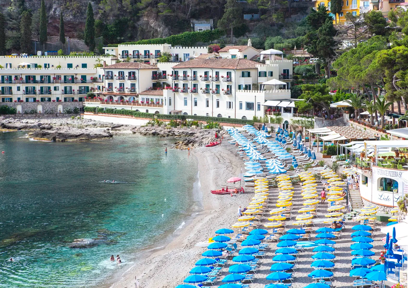 Beach scene with colorful umbrellas, buildings, and trees along a coastal area.