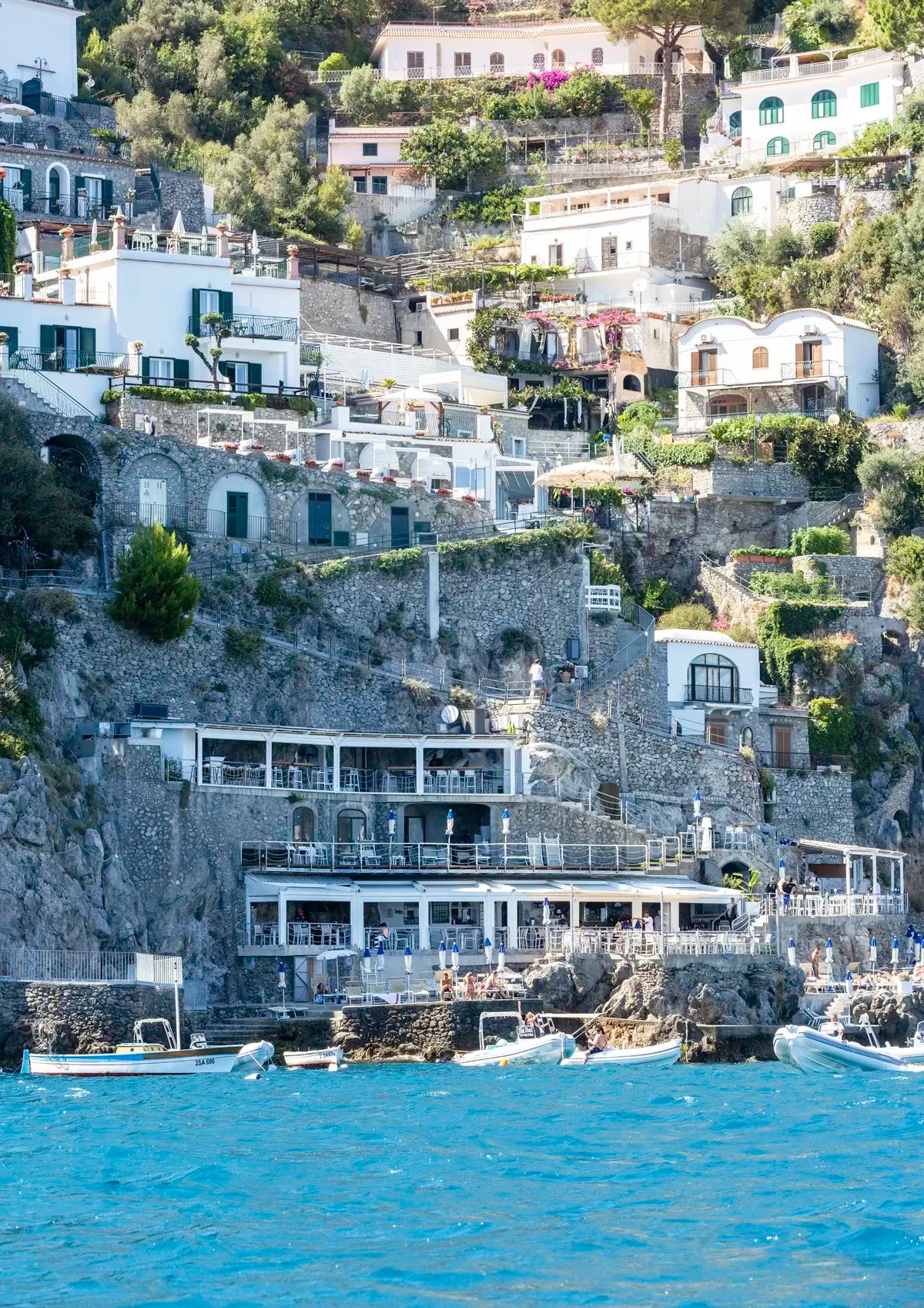 Hilly coastal town with white buildings and greenery, overlooking the sea.