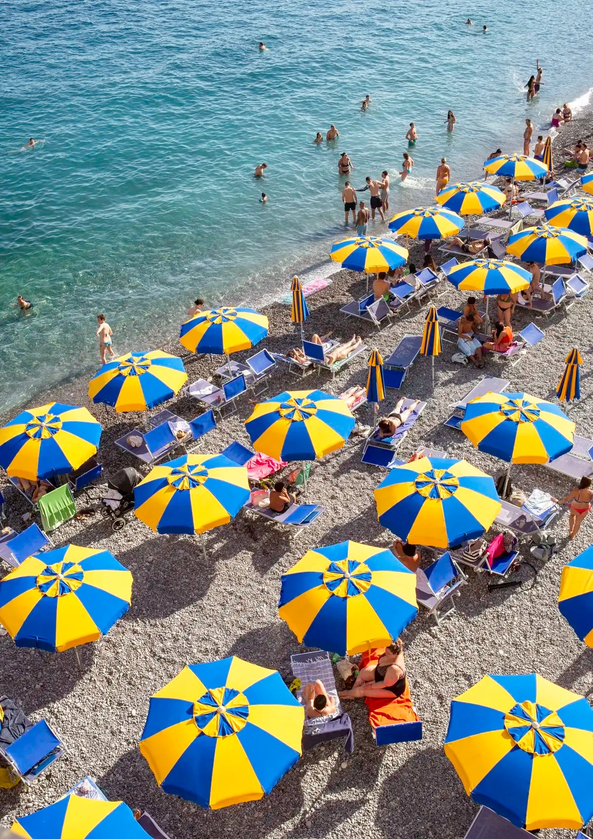 Beach scene with blue and yellow umbrellas and people enjoying the sun.