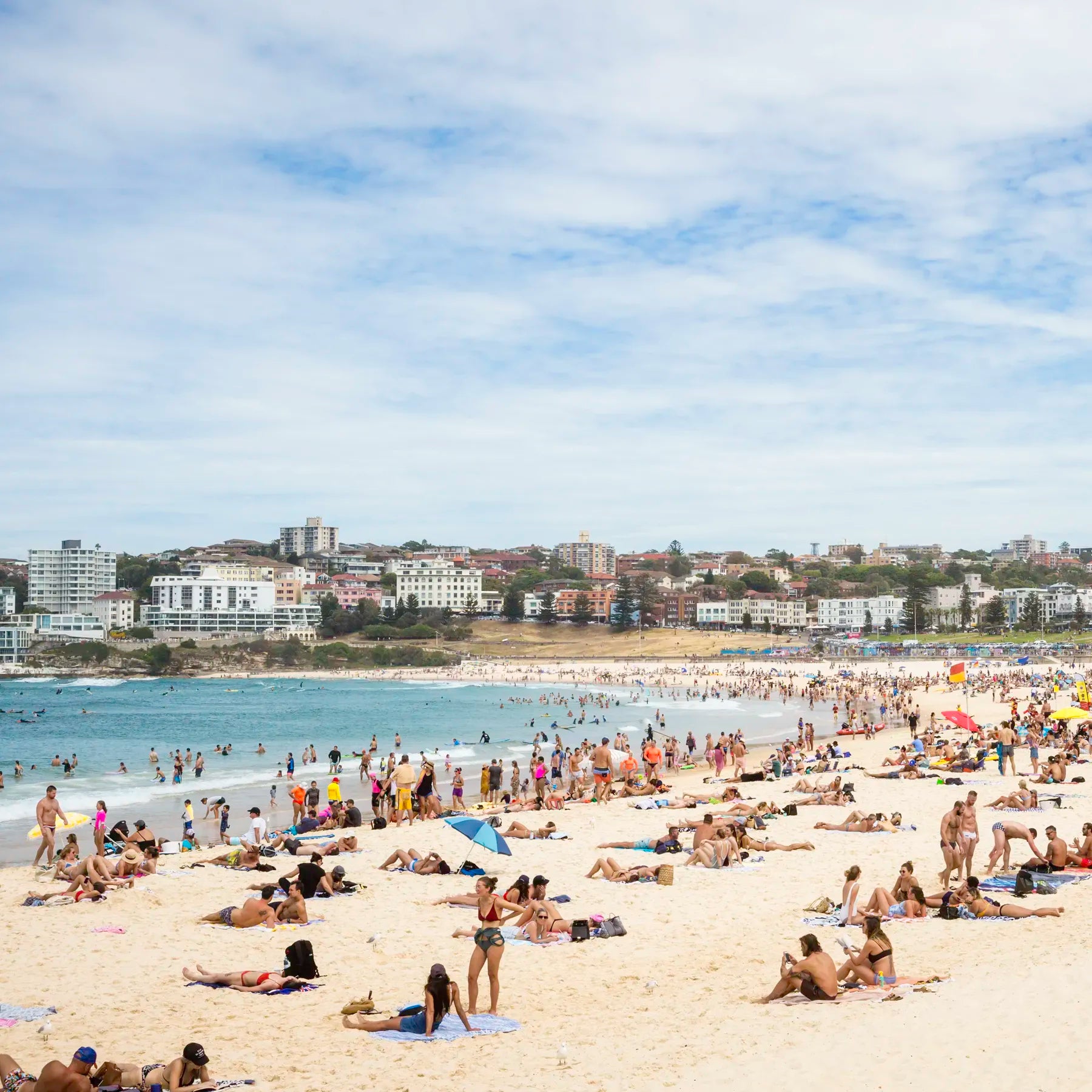 Beach scene with people sunbathing and swimming, buildings in the background