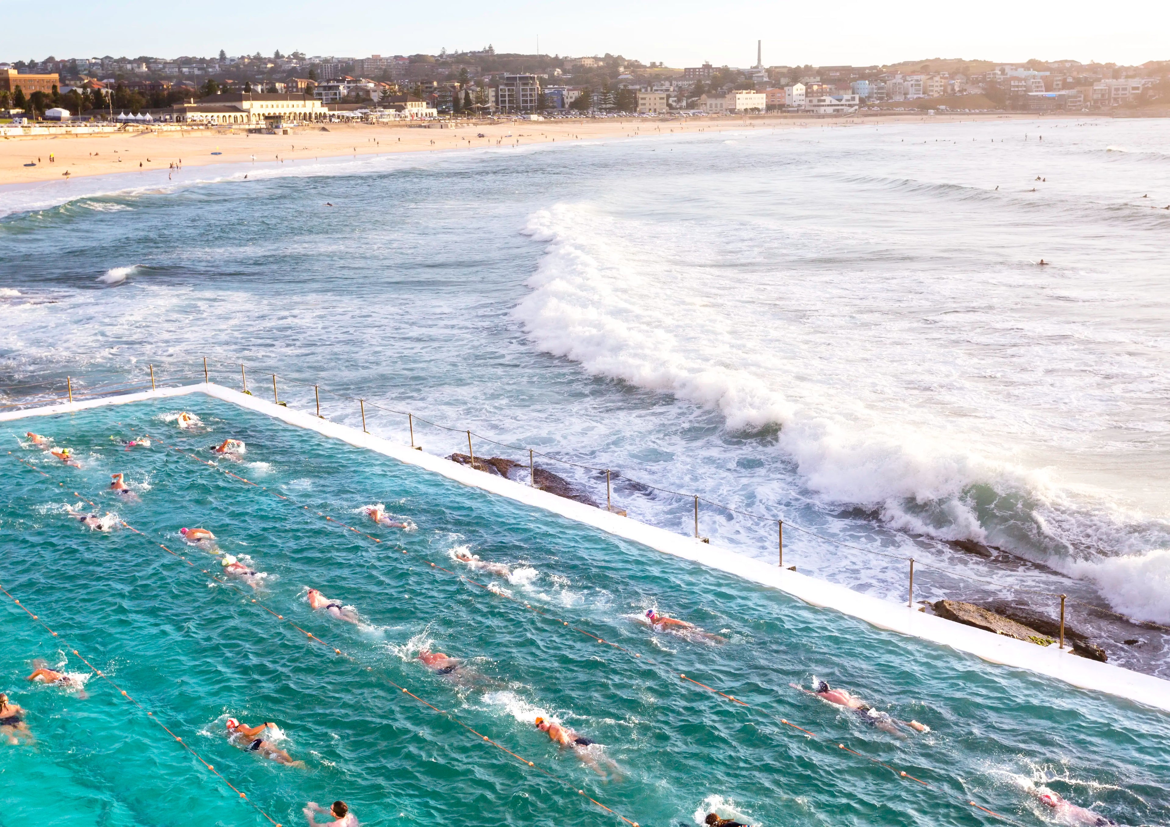 People swimming in a pool with ocean waves crashing onto the shore.