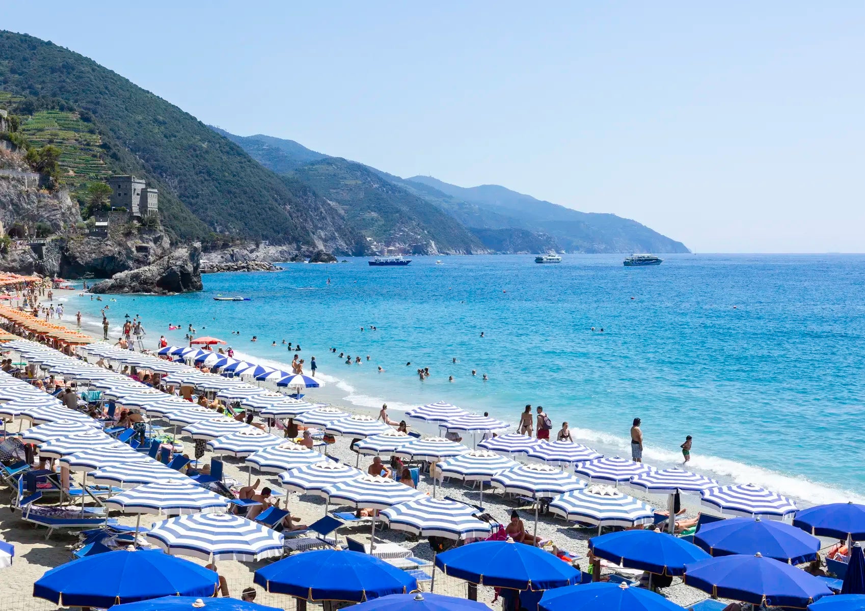 Beach scene with blue umbrellas, white towels, and people enjoying the sun by the sea.