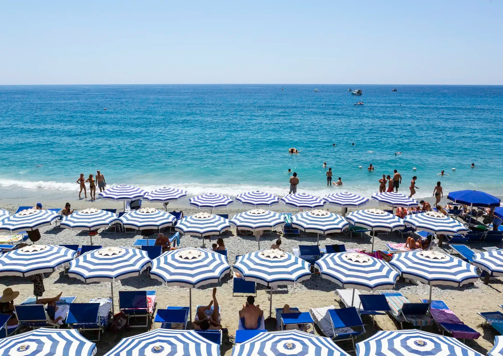 Beach scene with blue and white striped umbrellas and people enjoying the sun and water.