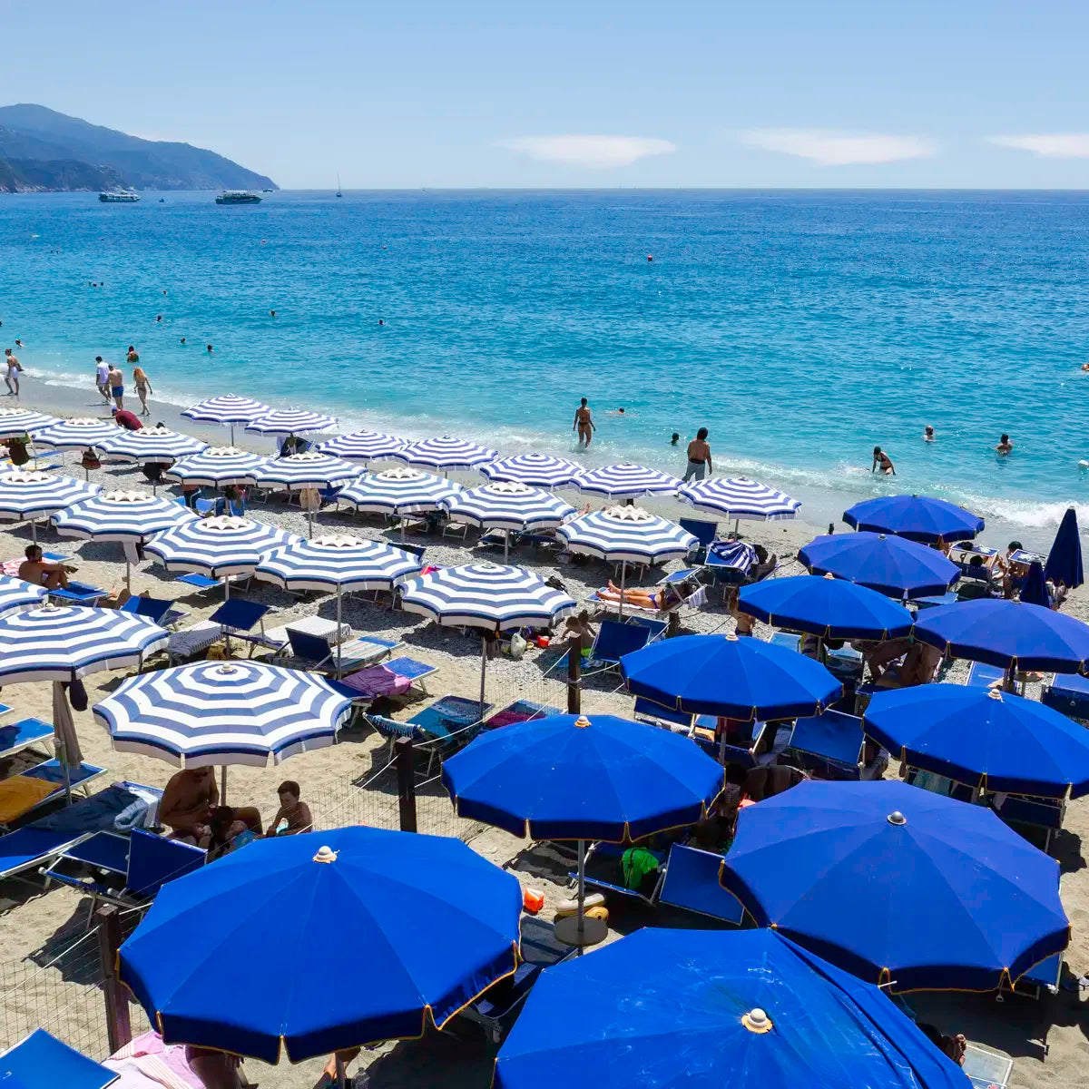 Beach scene with blue and white umbrellas and people enjoying the sun and water.