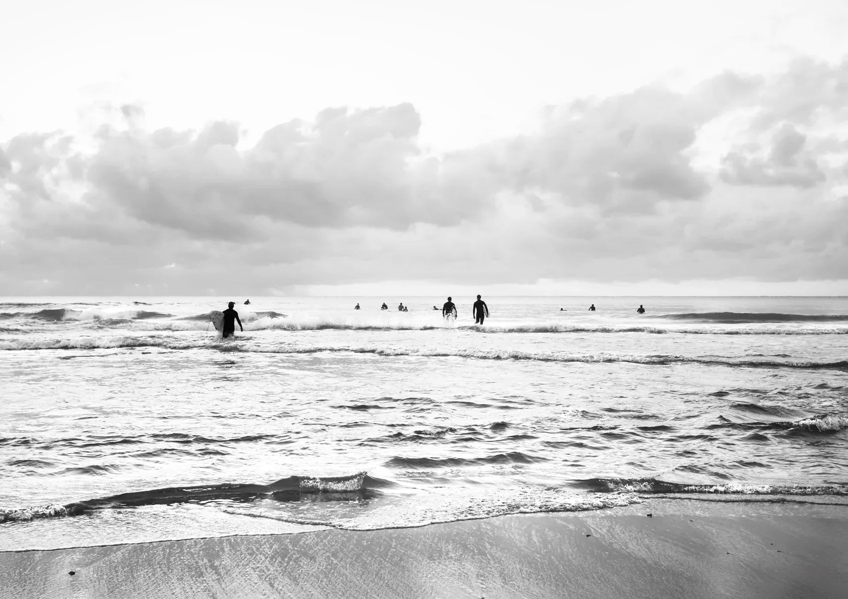 Black and white photo of people walking along a beach with a cloudy sky.