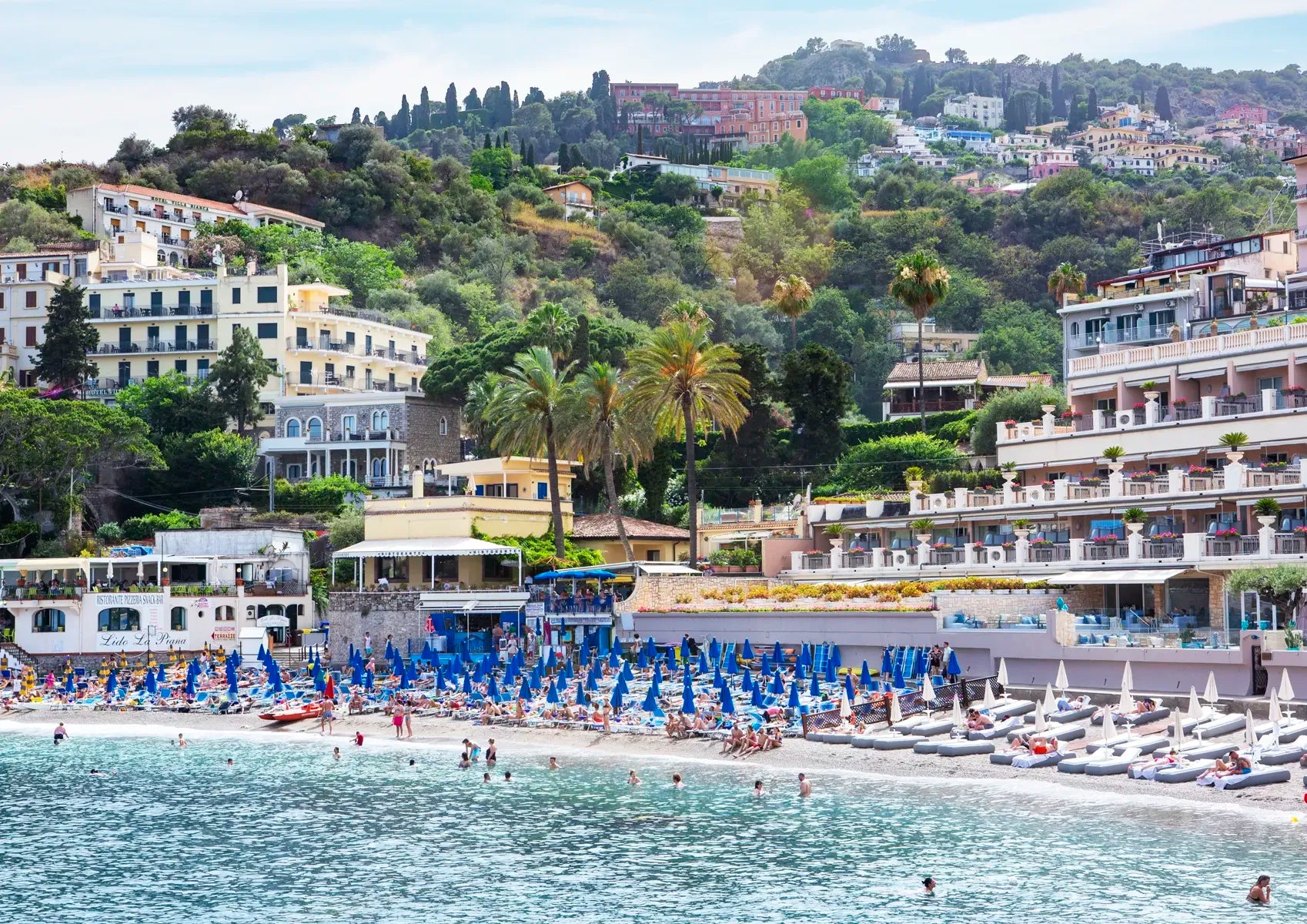 Beach scene with buildings, palm trees, and people in a coastal area.