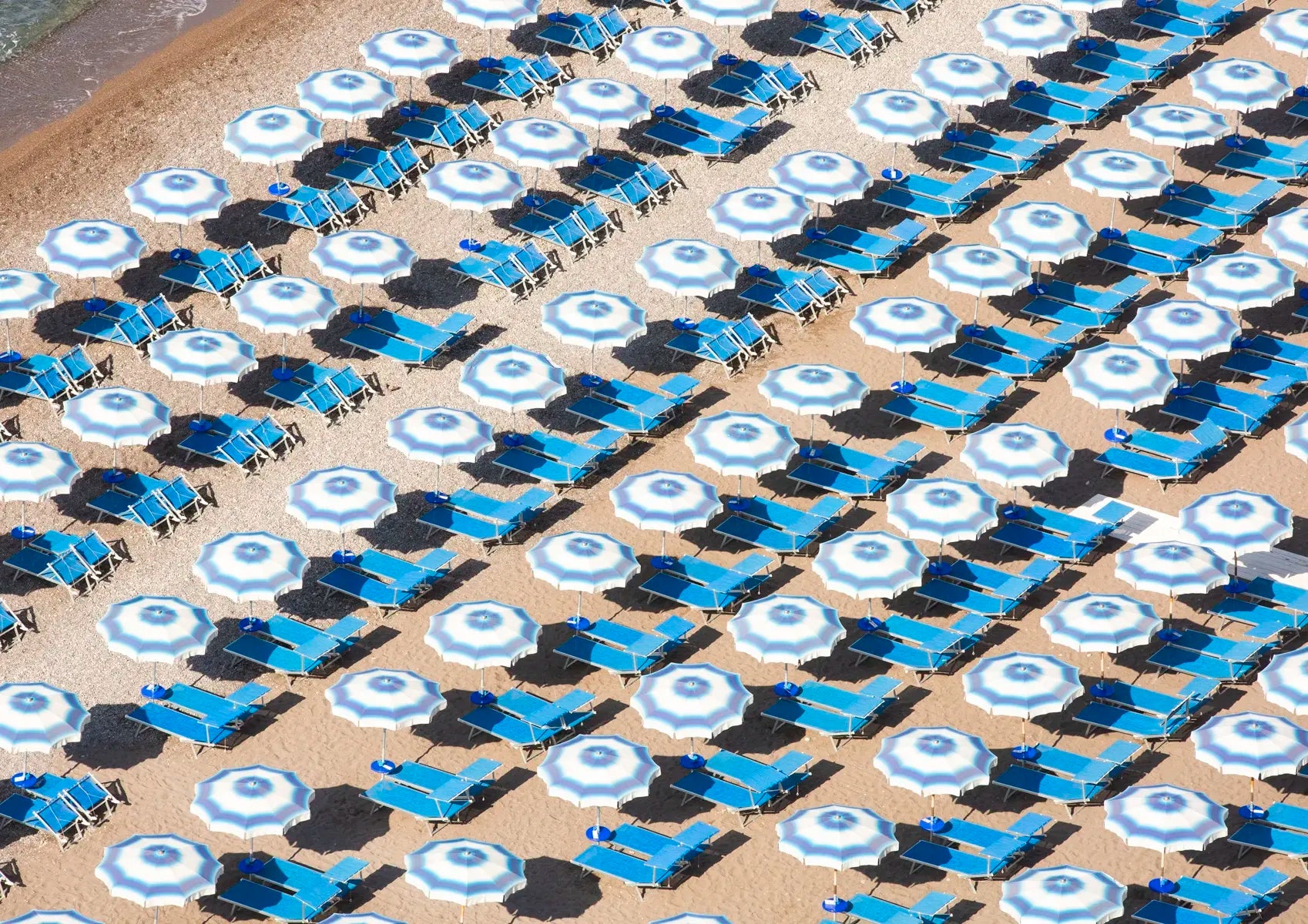 Pattern of blue and white umbrellas and lounge chairs on a sandy beach.