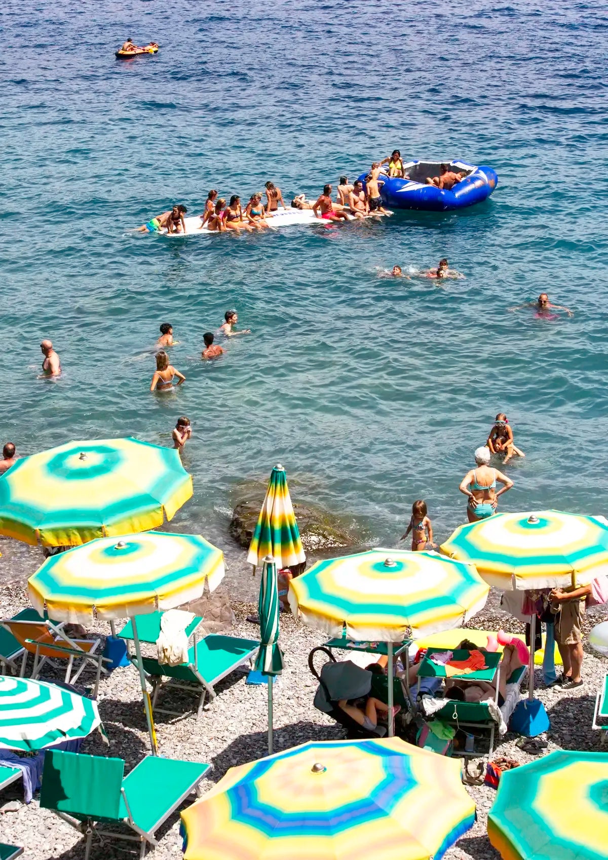 People enjoying the beach with colorful umbrellas and boats in the water.
