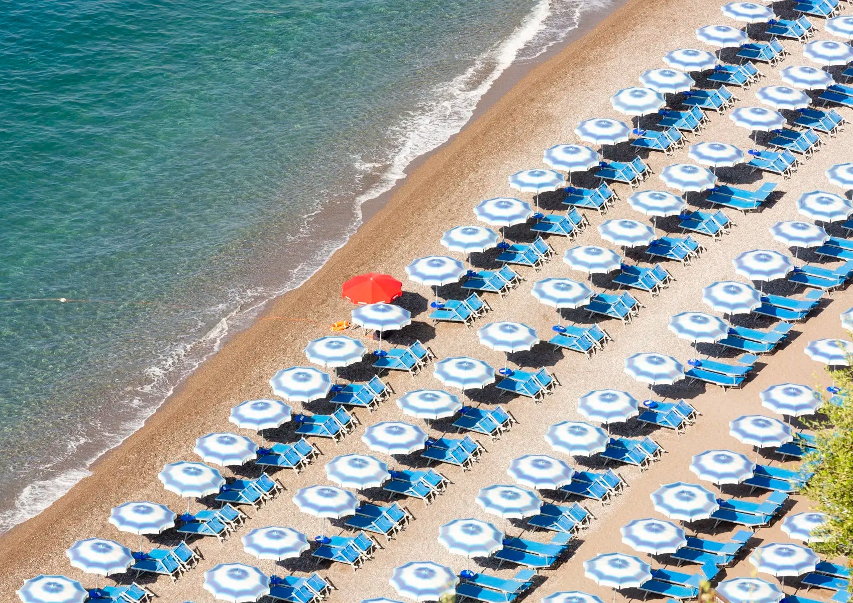 Beach scene with rows of blue and white umbrellas and a red umbrella.