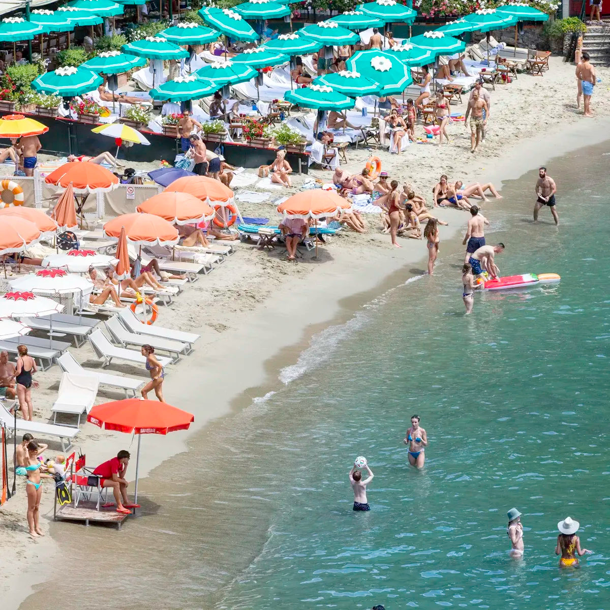 Beach scene with people sunbathing, swimming, and under umbrellas.