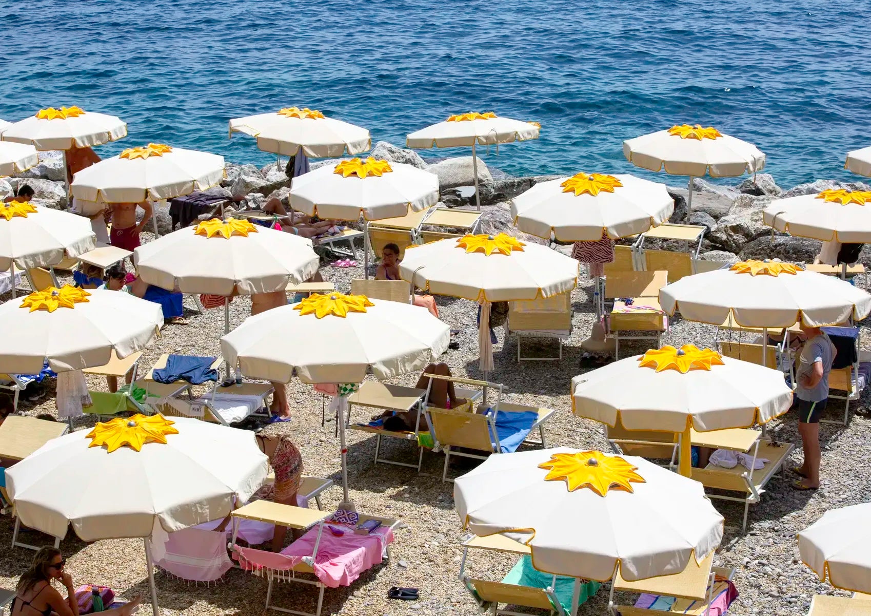 Beach scene with white and yellow umbrellas next to the ocean.