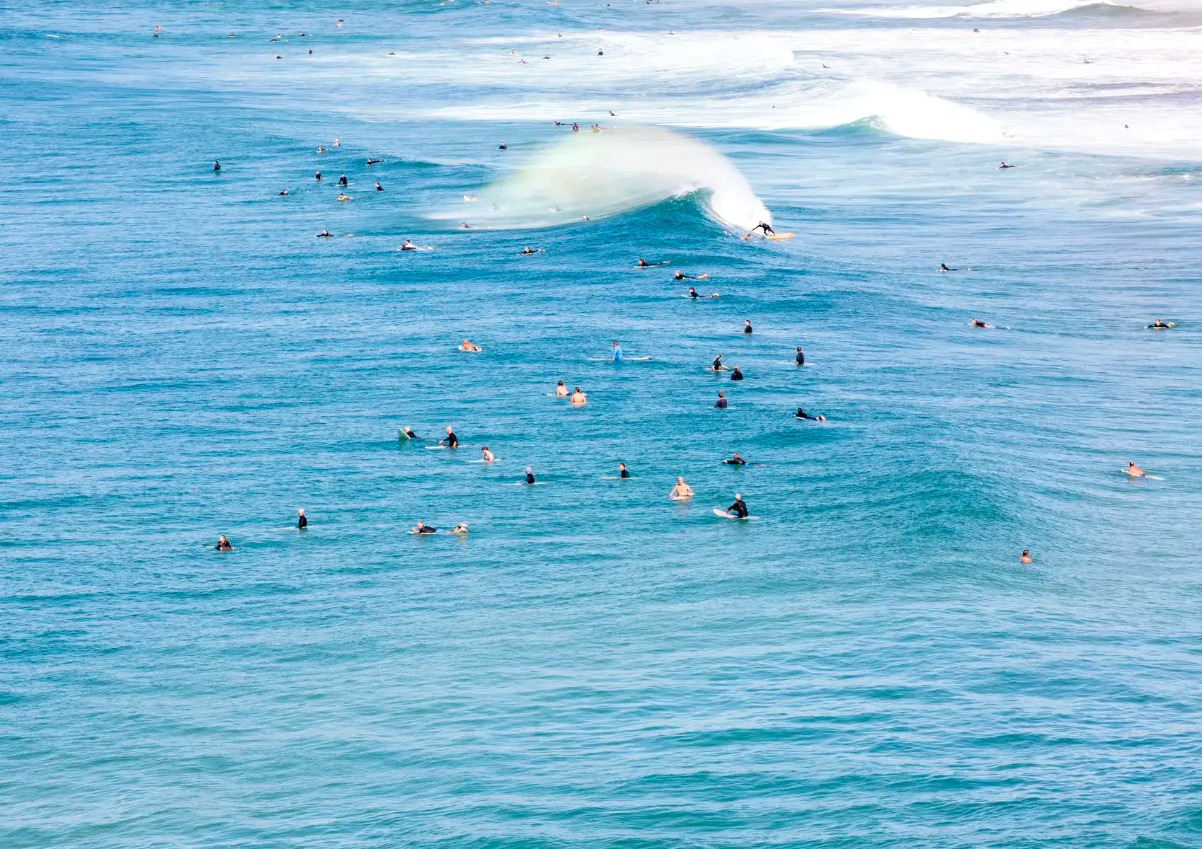 Surfers waiting for waves in a blue ocean with a large wave forming.
