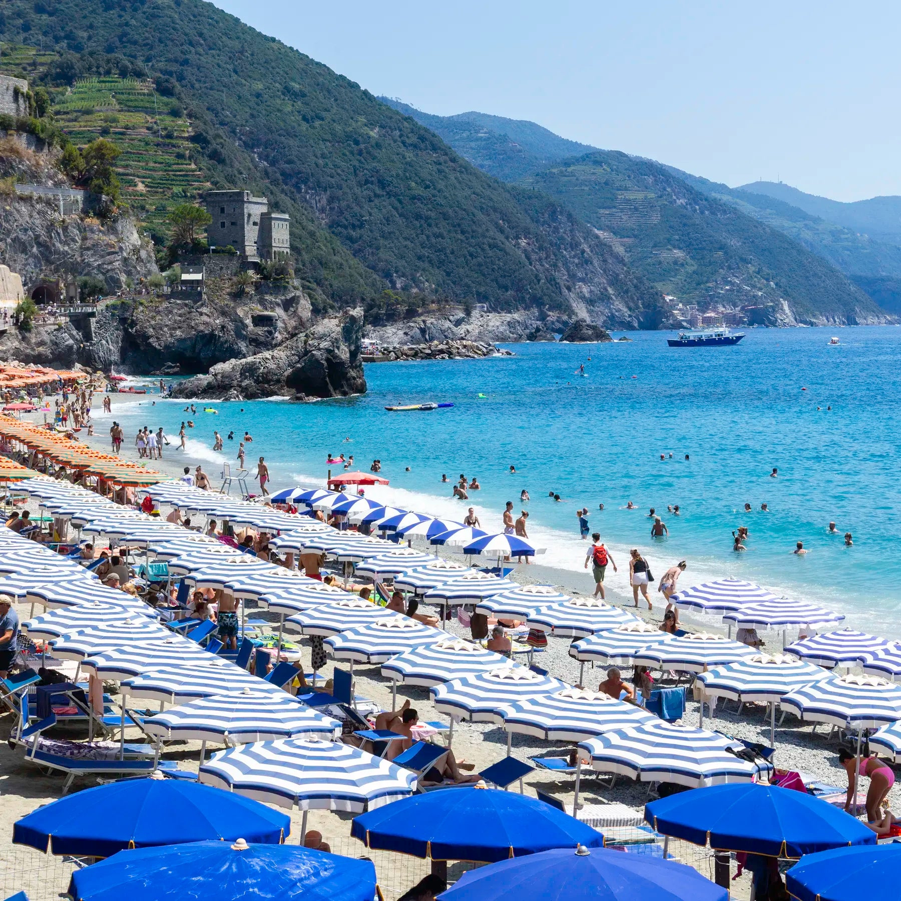 Beach scene with blue umbrellas, white towels, and people enjoying the sun on a mountainous island.