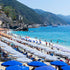 Beach scene with blue umbrellas, white towels, and people enjoying the sun on a mountainous island.
