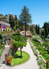 Stately garden with manicured lawns, pathways, and a large tree under a clear blue sky.
