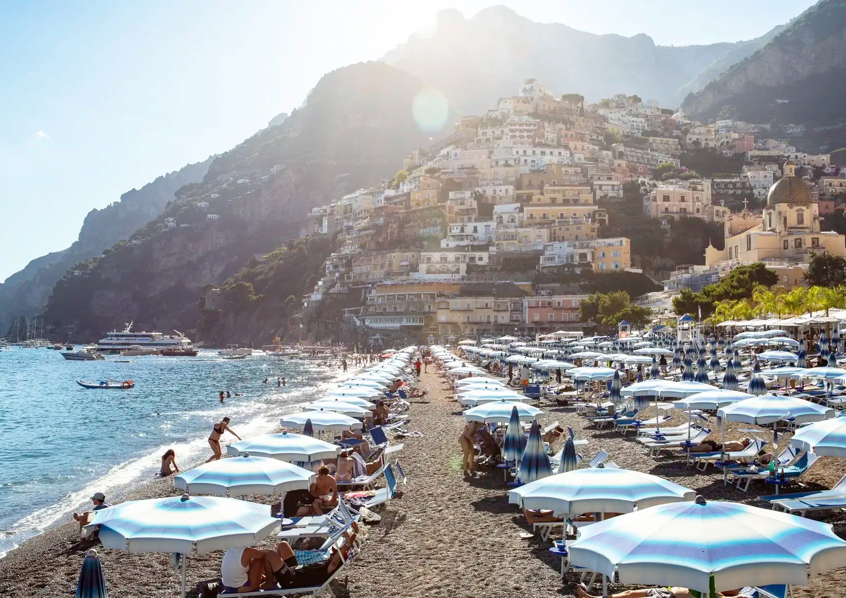 Beach scene with umbrellas, people, and a mountainous background