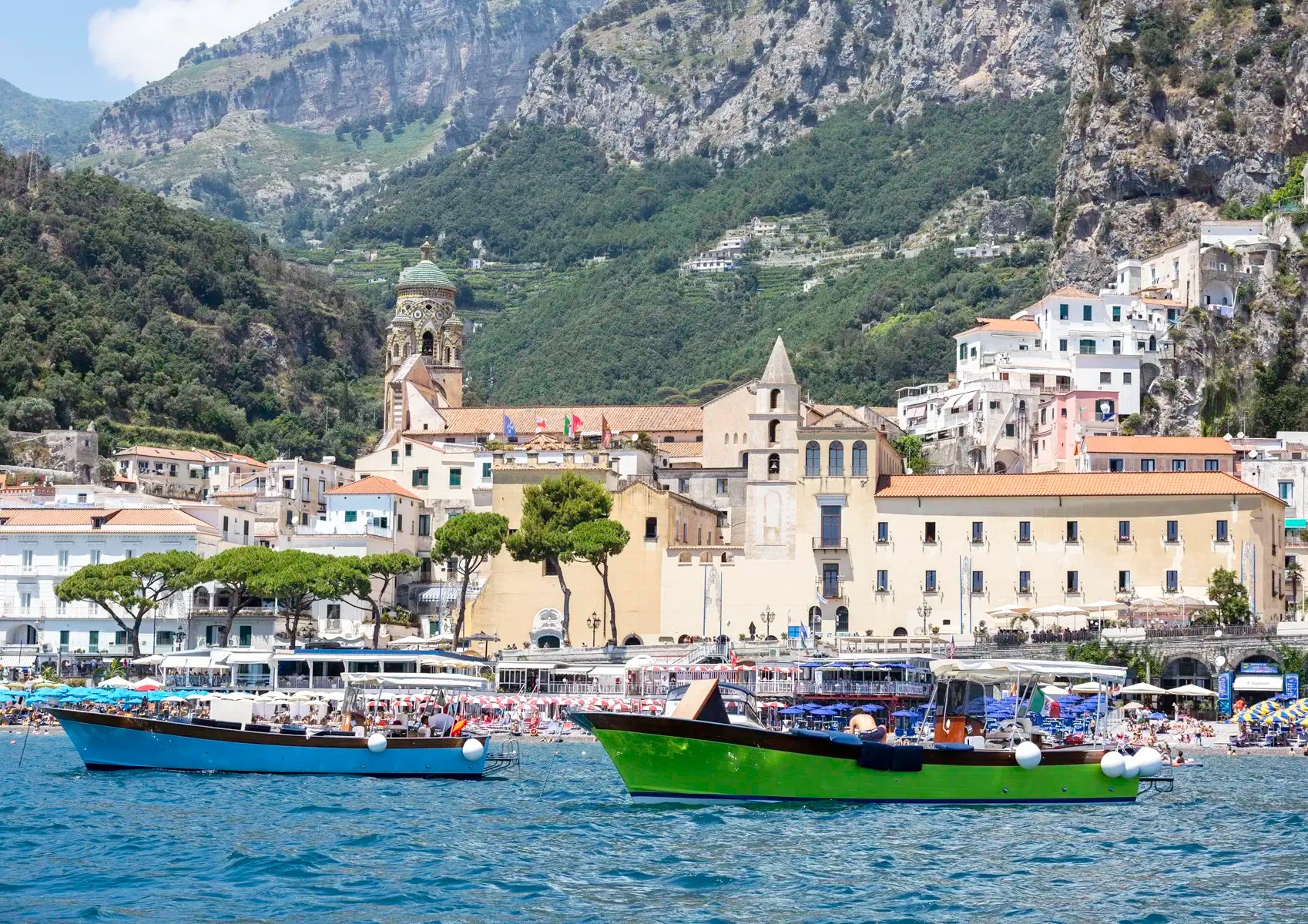 Villages by the sea with mountains in the background and the ocean in the foreground with boats in it.