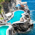 Luxury pool and lounge area on a rocky cliff overlooking the ocean with people around.