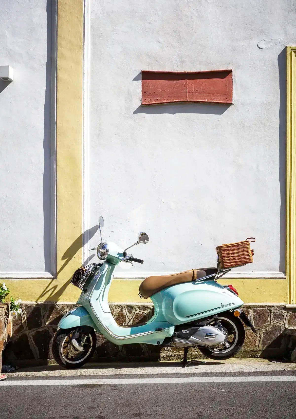 Light blue scooter with a basket on a street next to a building
