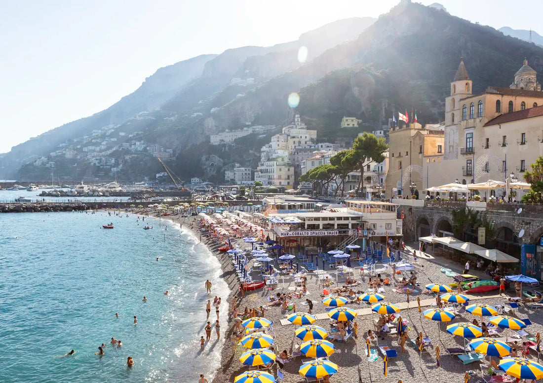 Beach scene with umbrellas, people, and buildings with mountains in the background