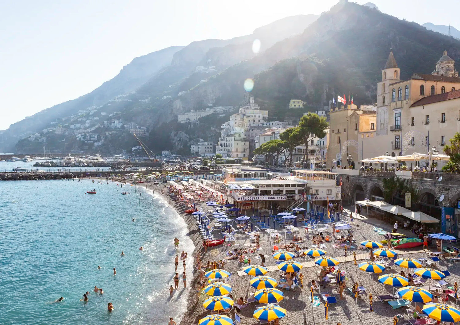 Beach scene with umbrellas, people, and buildings with mountains in the background