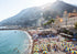 Beach scene with umbrellas, people, and buildings with mountains in the background
