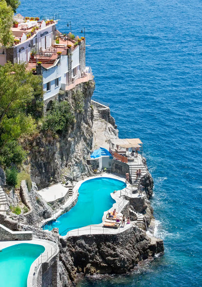 Houses built on a cliff overlooking the ocean with a pool.