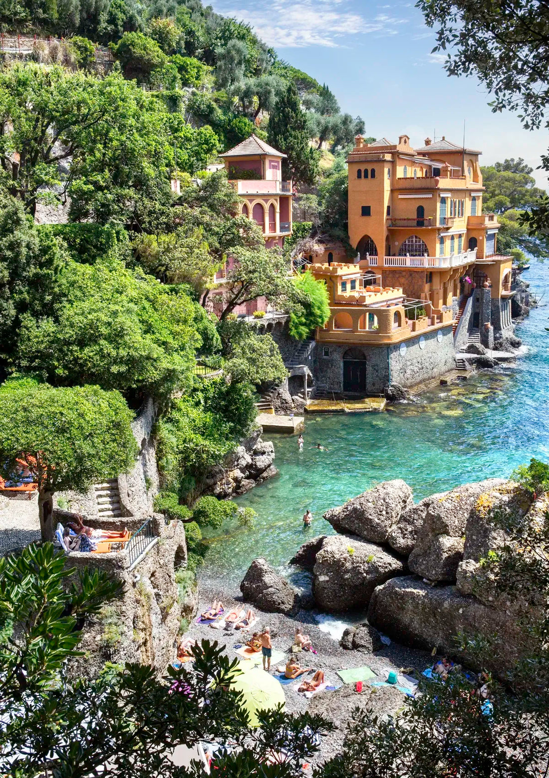 Luxurious waterfront villa in Portofino with gardens and a pool, surrounded by trees and rocks.