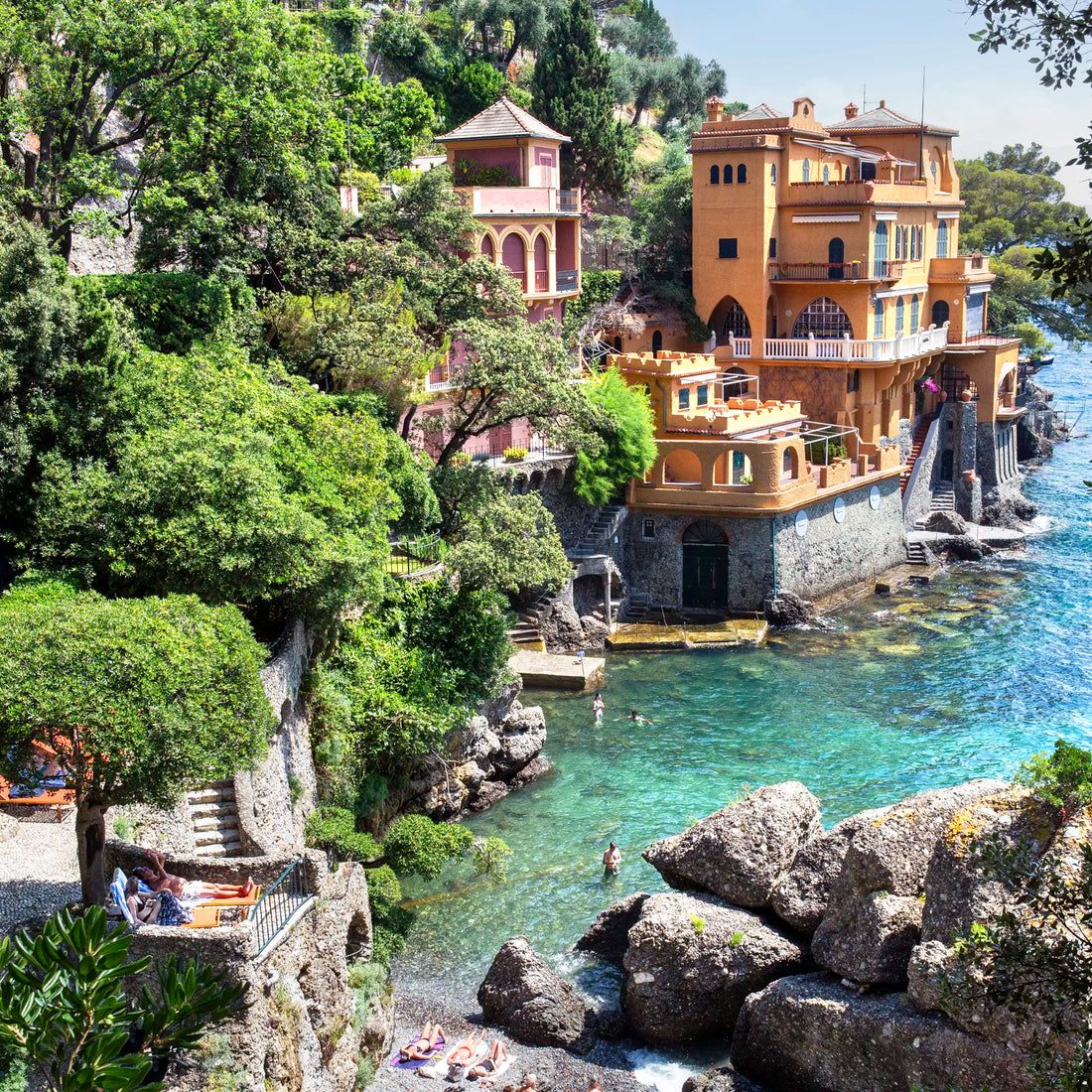 Luxurious waterfront villa with gardens and a pool, surrounded by trees and rocks.