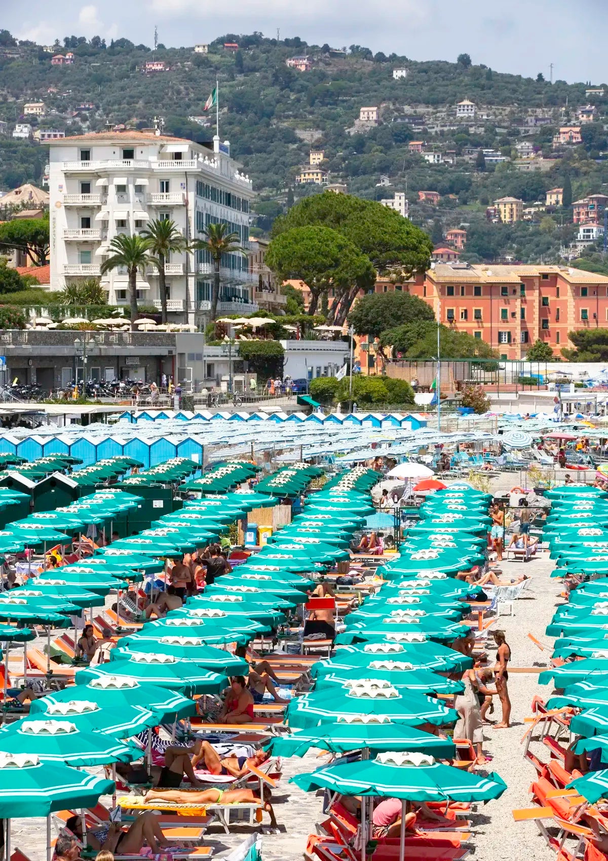 Beach scene with rows of green umbrellas and people under a cloudy sky.