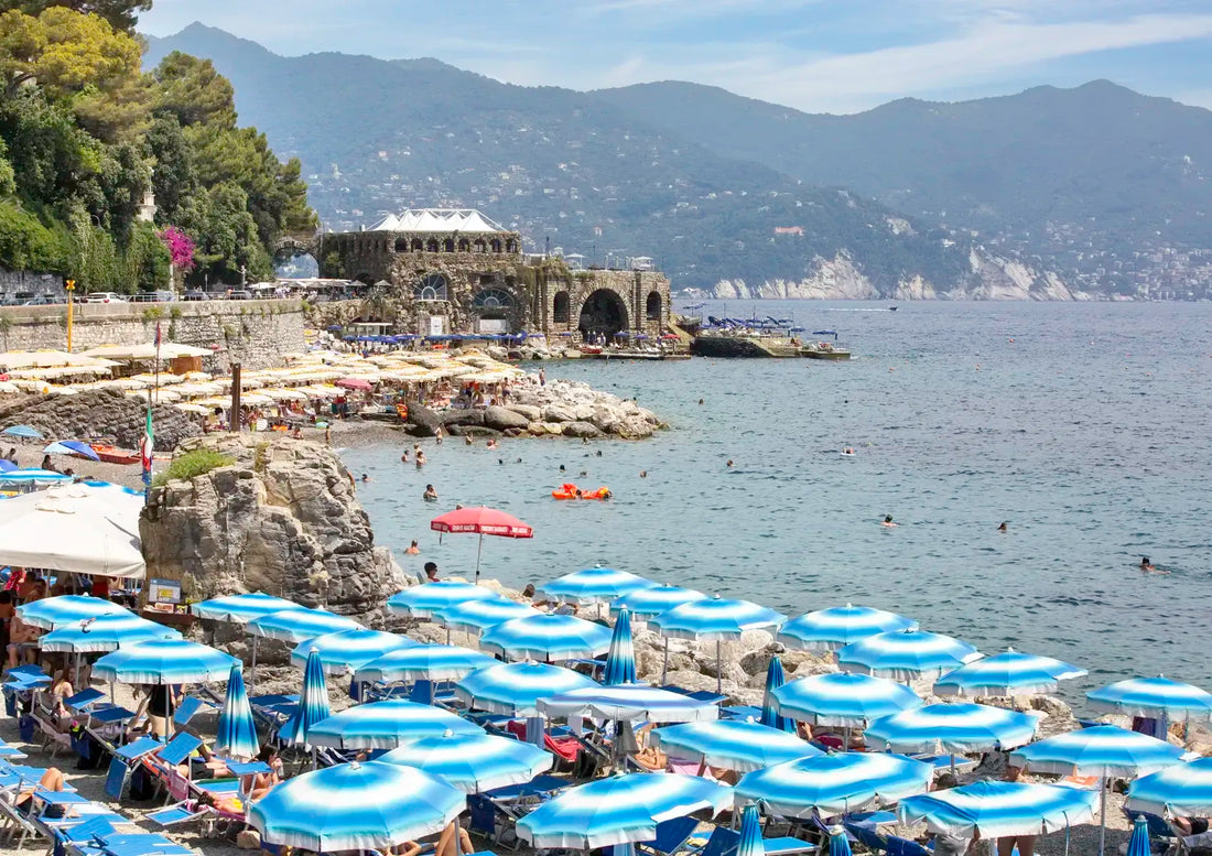 Beach scene with blue umbrellas, people, and a mountainous background.