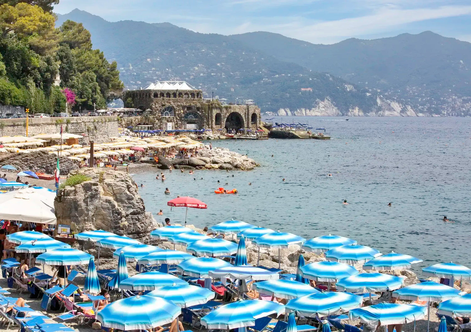 Beach scene with blue umbrellas, people, and a mountainous background.