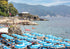 Beach scene with blue umbrellas, people, and a mountainous background.