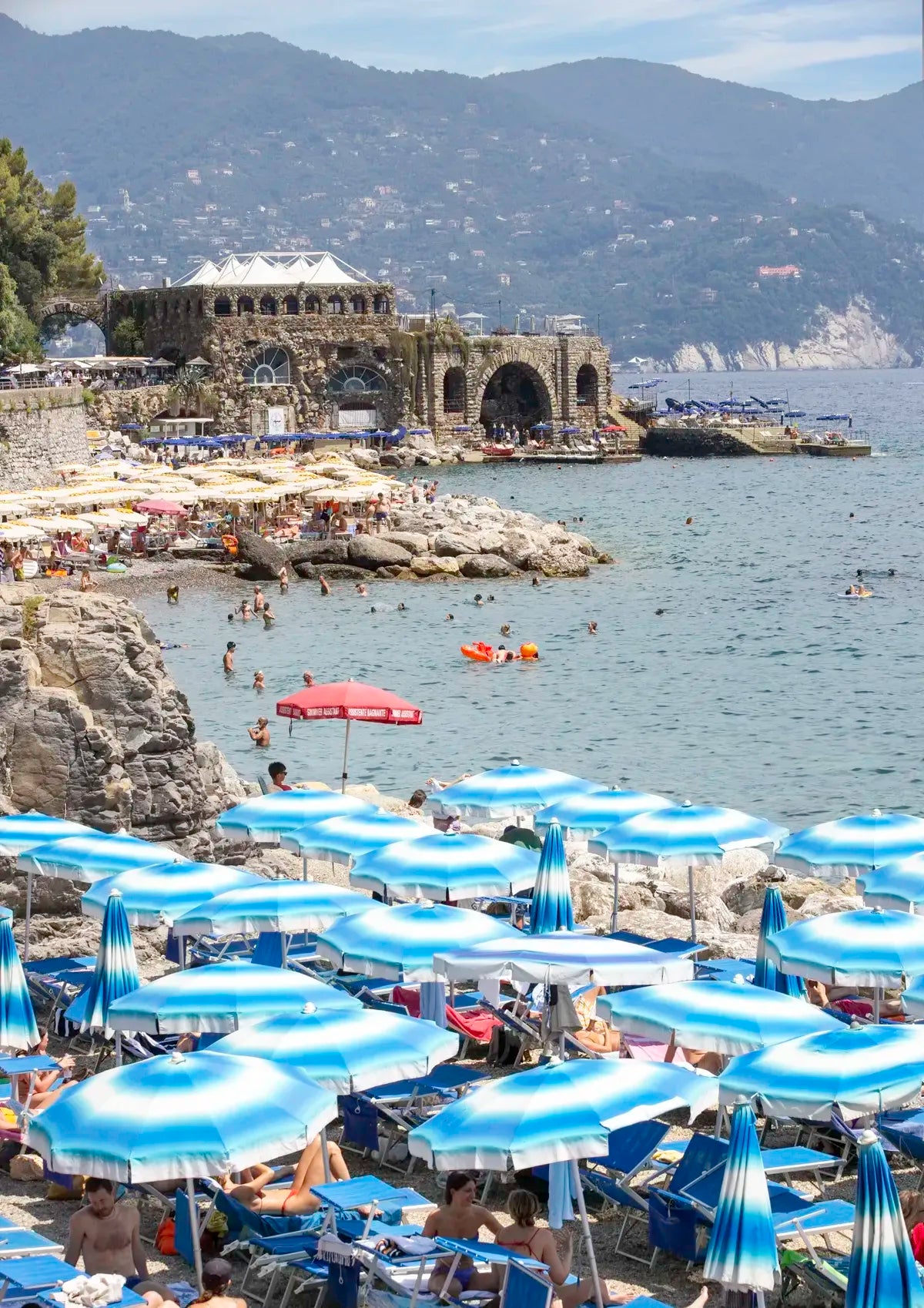Beach scene with blue umbrellas, people, and a coastal building.