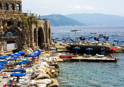 Coastal scene with stone building, umbrellas, and boats near water