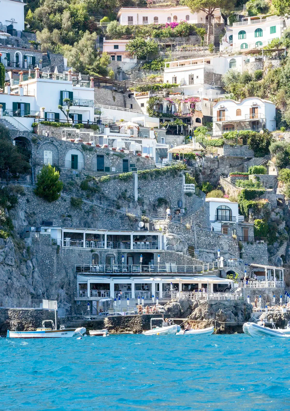 Hilly coastal town with white buildings and greenery, overlooking the sea.