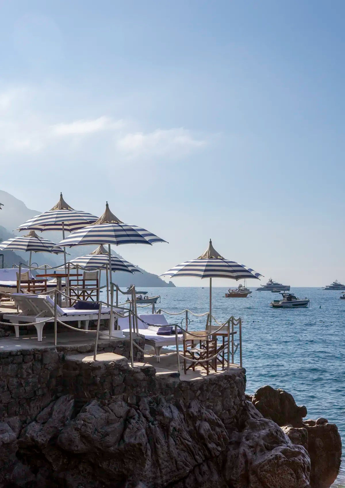 Beachside setting with striped umbrellas and chairs overlooking the ocean with boats.