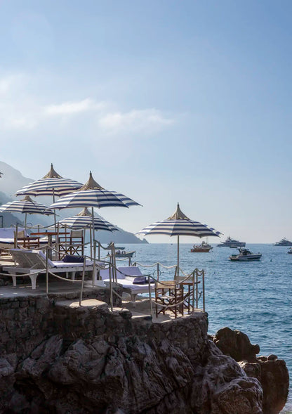 Beachside setting with striped umbrellas and chairs overlooking the ocean with boats.