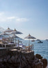 Beachside setting with striped umbrellas and chairs overlooking the ocean with boats.