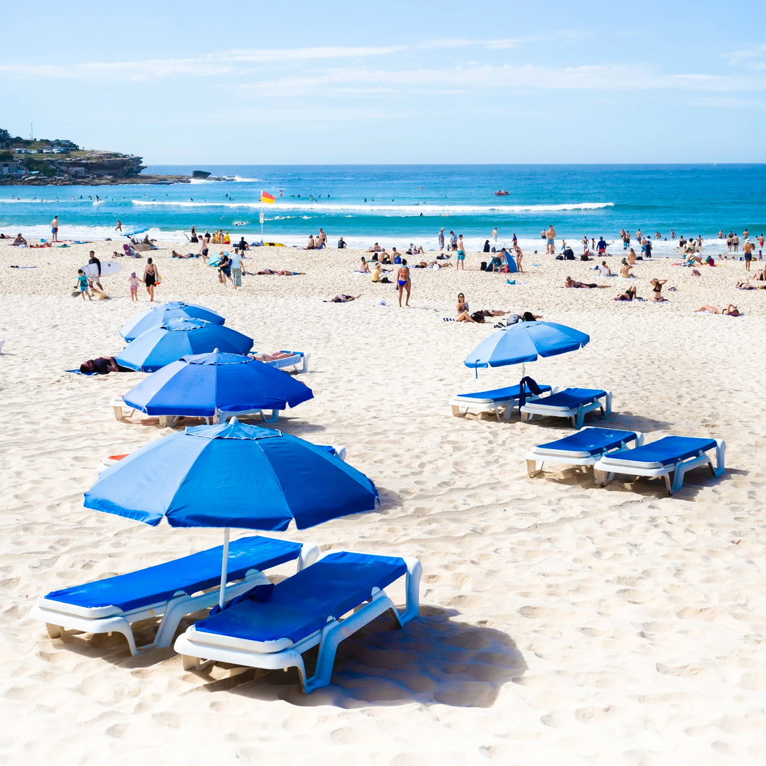 Beach scene at Bondi beach with blue umbrellas and lounge chairs on a sandy shore.