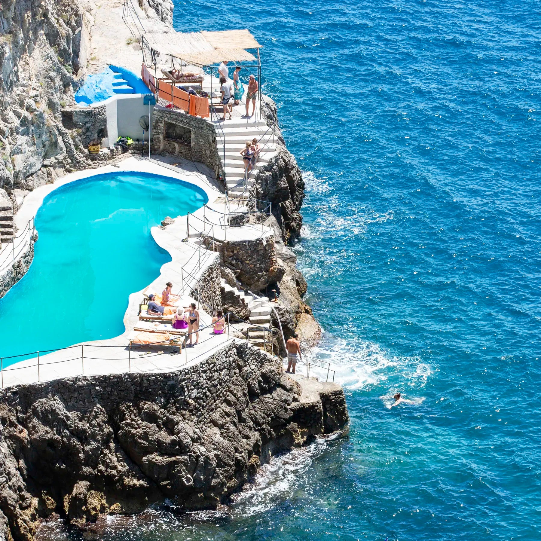 Pool built into a rocky cliffside with people around, overlooking the ocean.