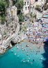 People enjoying a beach with historical architecture and boats in the background.