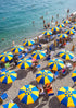 Beach scene with blue and yellow umbrellas and people enjoying the sun.