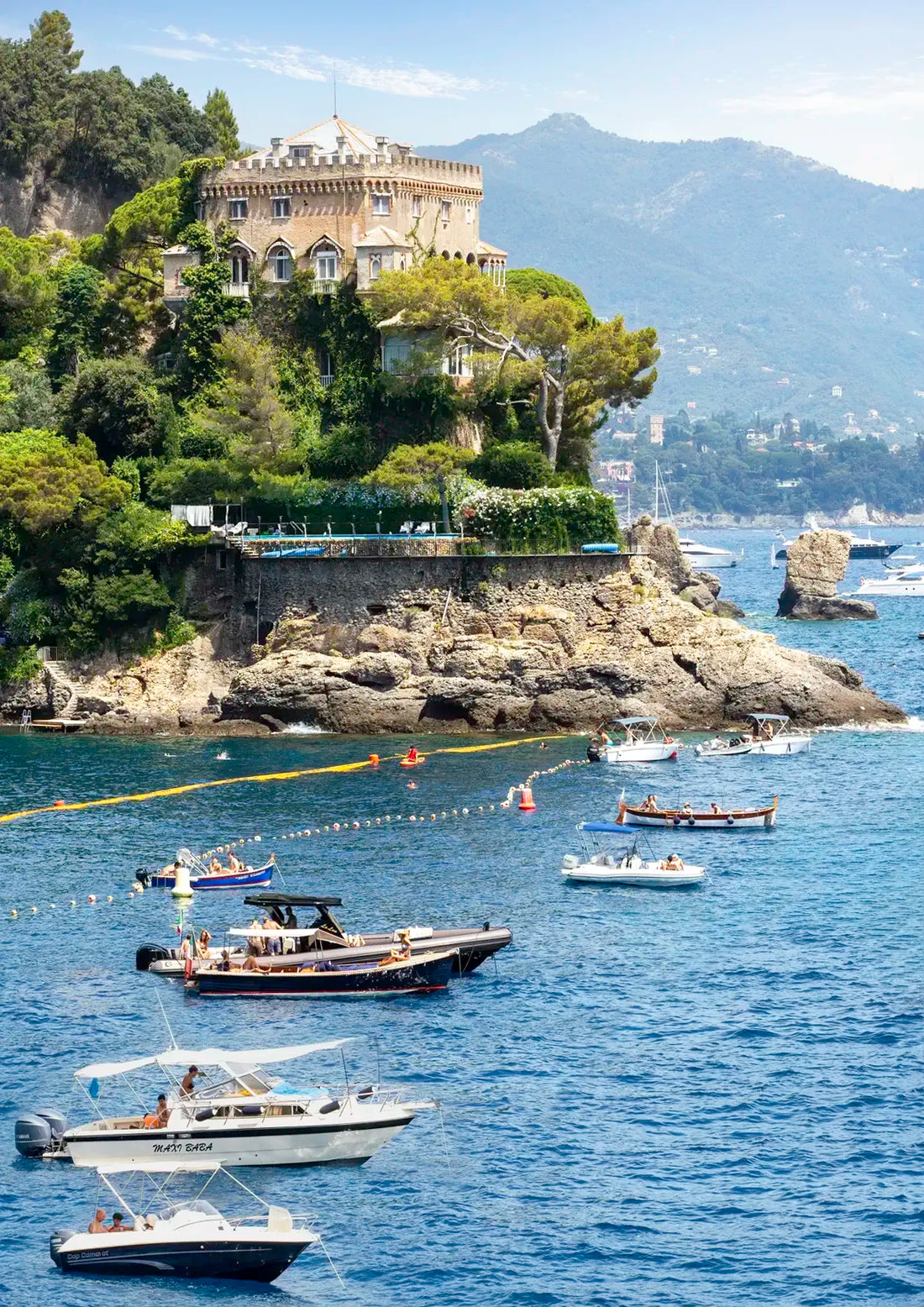 Boats in the water near a castle on a cliff with mountains in the background