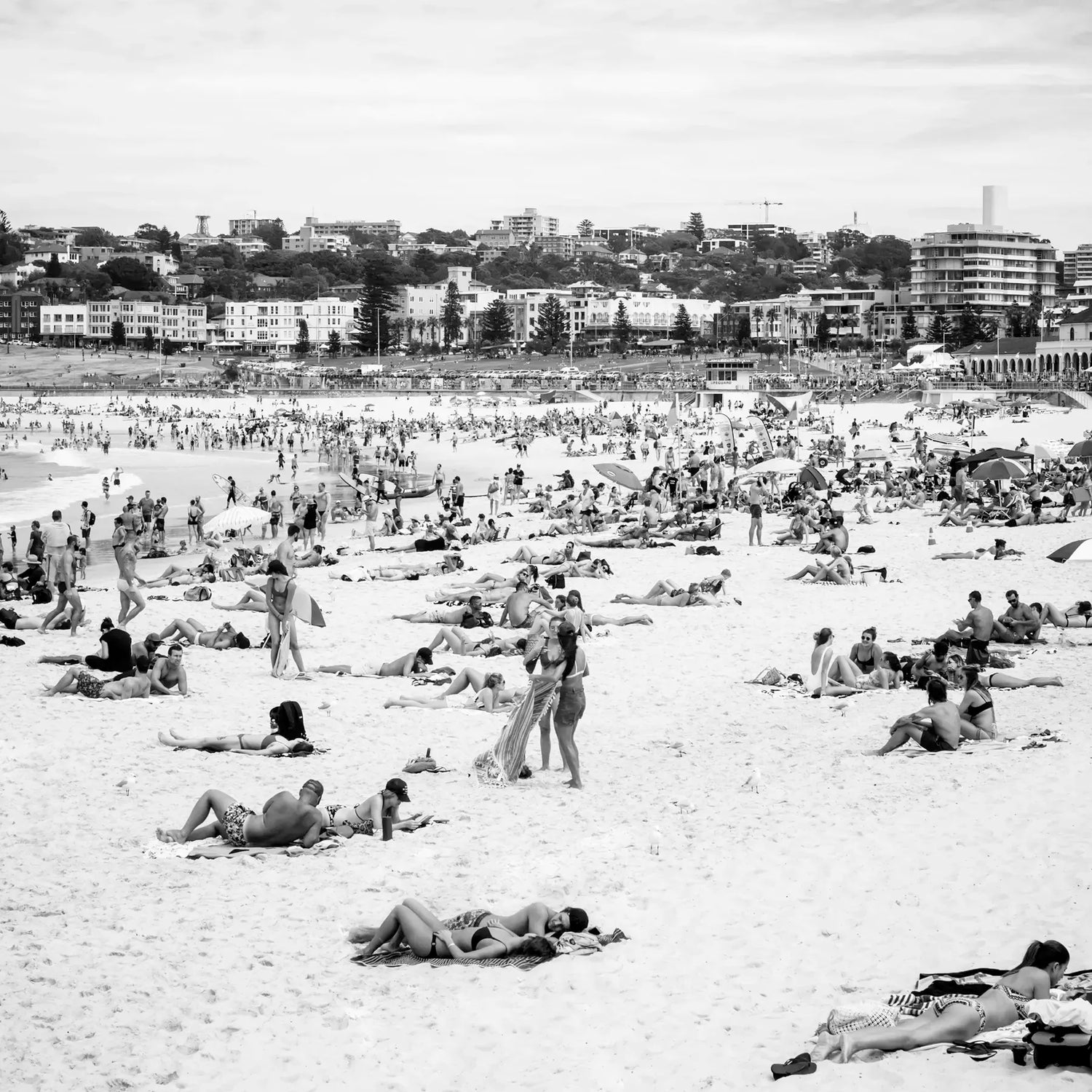  crowded beach with people sunbathing and relaxing, with buildings in the background