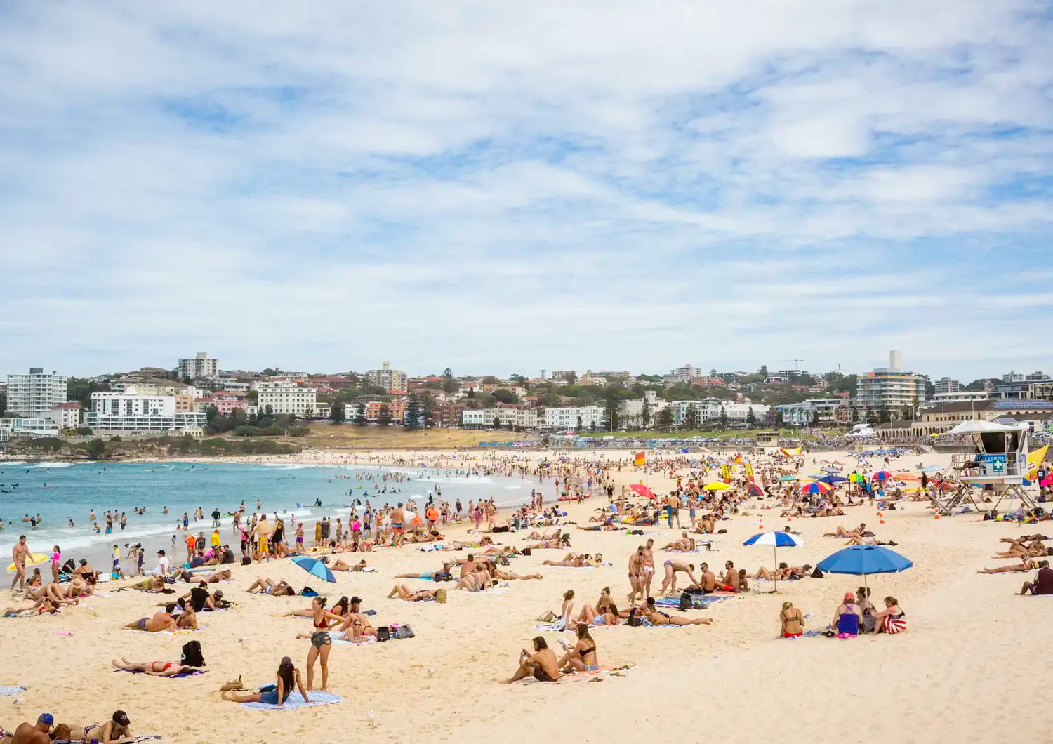Beach scene with people, umbrellas, and buildings in the background