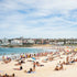 Beach scene with people sunbathing and swimming, buildings in the background