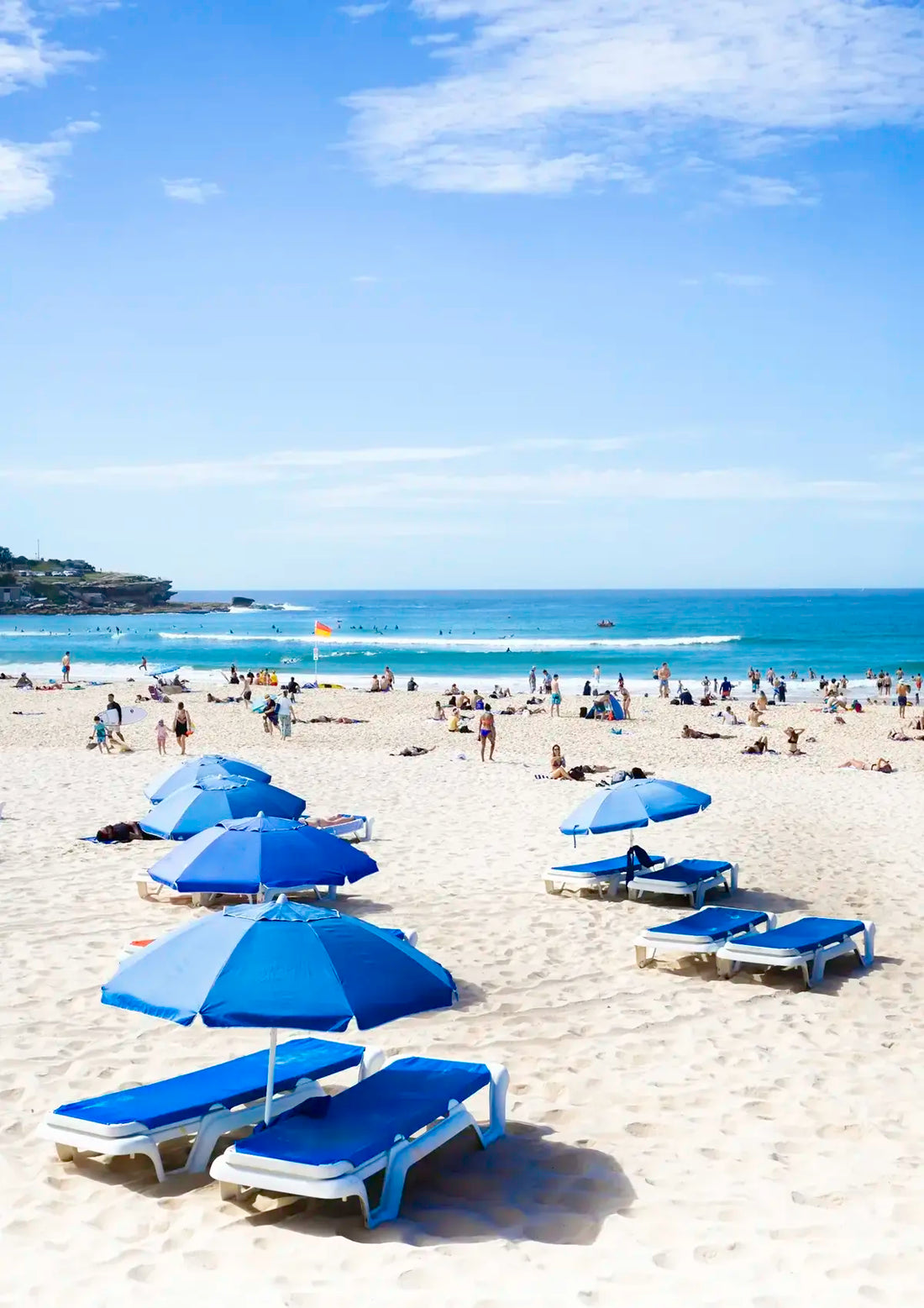 Beach scene with blue umbrellas and lounge chairs under a clear sky.