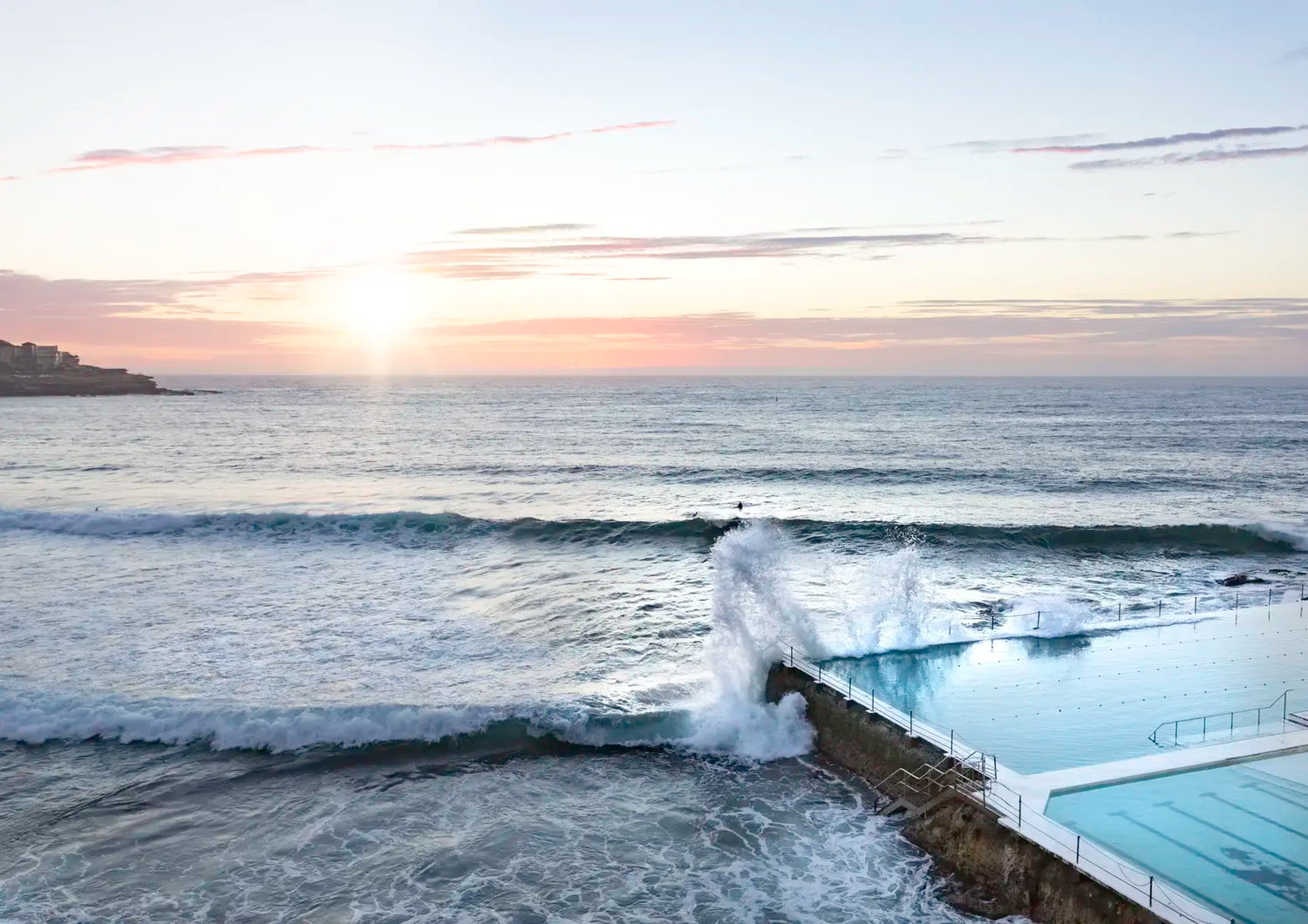 Ocean waves crashing against a wall with a sunset over the water.